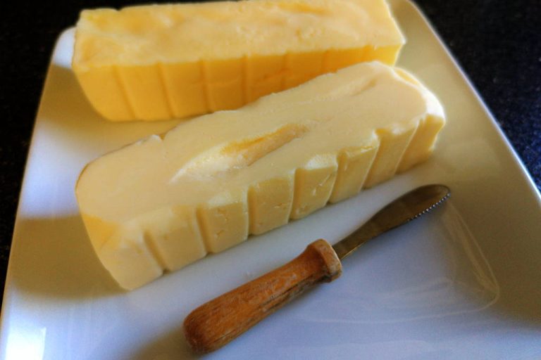 Two sticks of homemade butter sitting on a white square dish with a butter knife.
