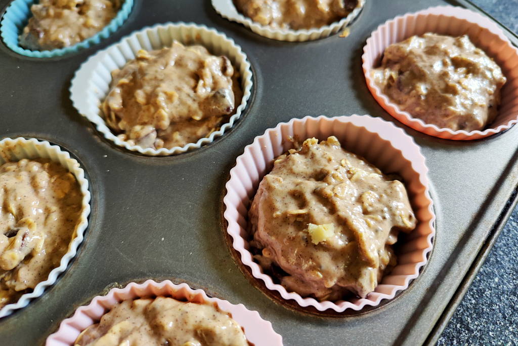 Sourdough oatmeal muffin dough inside silicone liners in a muffin tin, without topping.