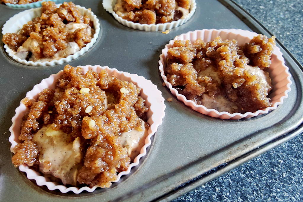 Sourdough oatmeal muffin dough with crumble topping inside silicone liners in a muffin tin.