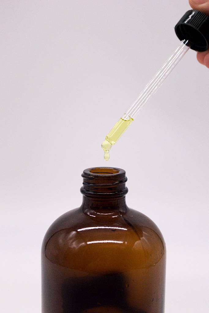 Amber-colored glass bottle with eyedropper dripping lemon essential oil into it.