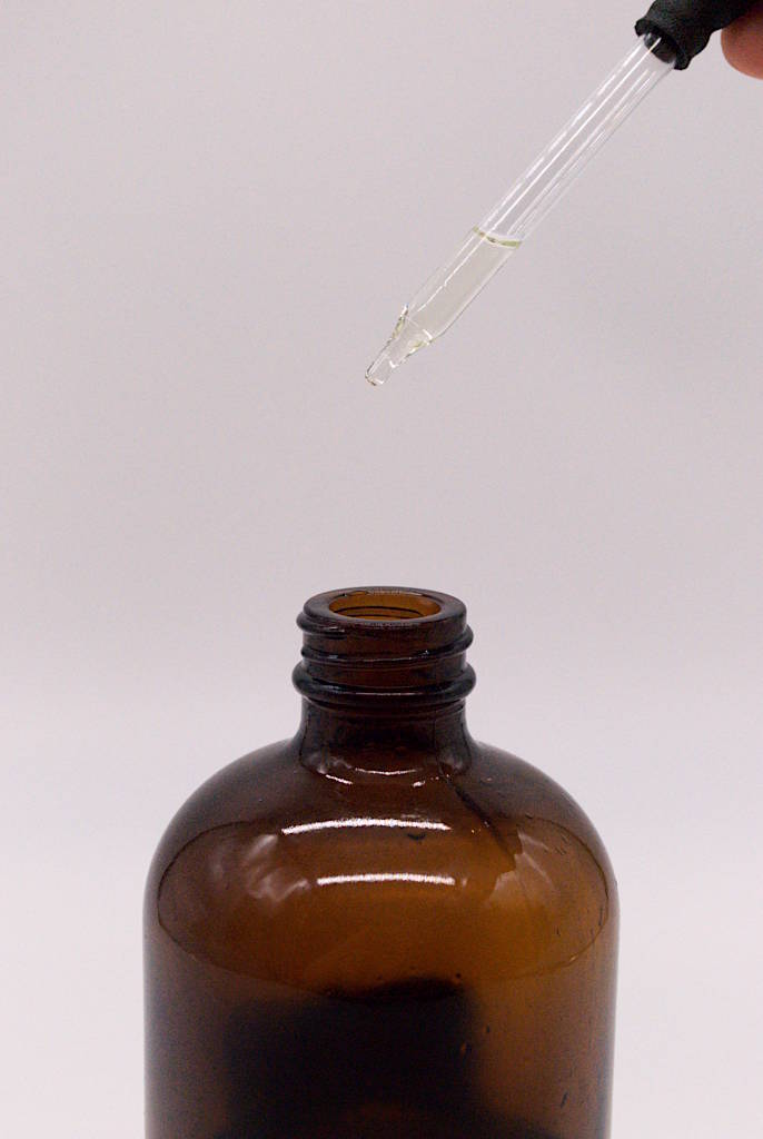 Amber-colored glass bottle with eyedropper dripping tea tree essential oil into it.