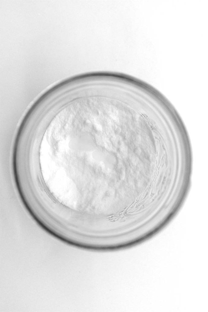 Bird's eye view of a mason jar with baking soda and essential oil added, unmixed.
