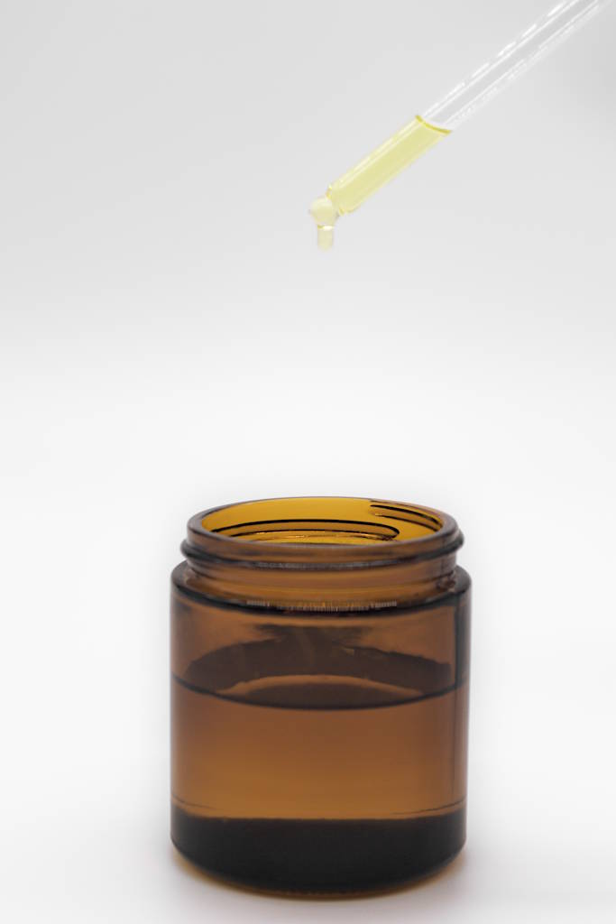 An amber-colored glass jar with oil inside and lemon essential oil being added to it.