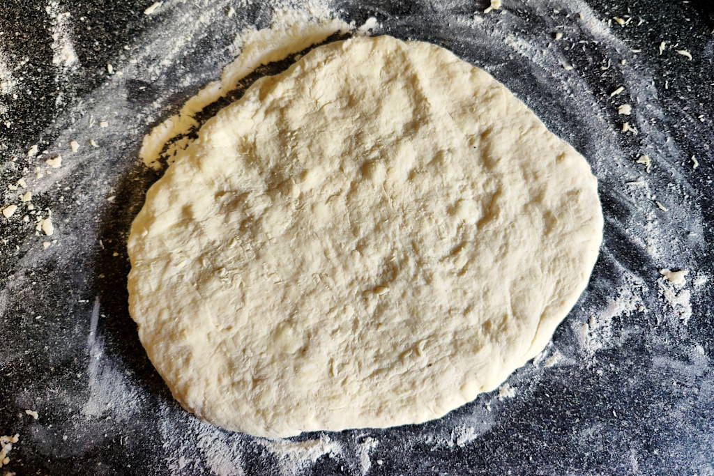Buttermilk biscuit dough patted out into a circular disk.