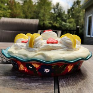 Strawberry lemon cream pie in a decorative pie dish sitting on a patio table outside.