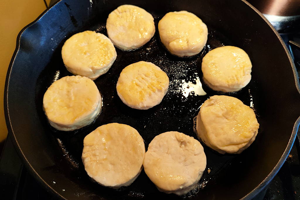 Nine buttermilk biscuits unbaked in a cast iron skillet with melted vegetable shortening.
